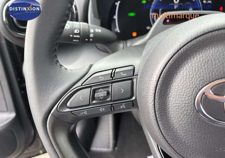 Gros plan sur le volant cuir gris de la Toyota Yaris Cross avec commandes multifonctions et tableau de bord numérique en arrière-plan.