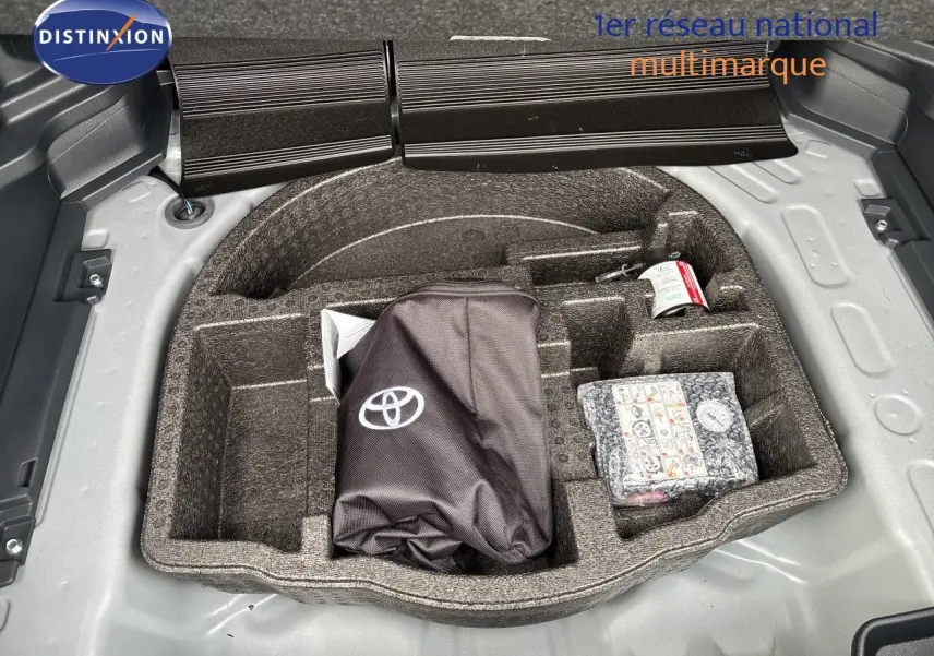 Coffre ouvert d'une Toyota Yaris Cross gris atlas métal, montrant le rangement sous plancher avec kit de secours et accessoires.