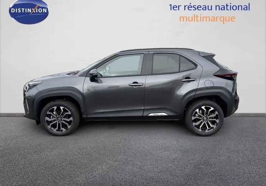 Vue de profil côté gauche d'une Toyota Yaris Cross gris atlas métal avec jantes alliage bicolores et logo sur bas de porte.