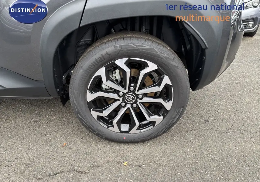 Gros plan sur la roue avant gauche d'une Toyota Yaris Cross gris atlas métal, mettant en valeur la jante alliage bicolore.