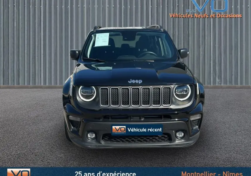 Jeep Renegade noir vue de face, avec calandre à sept fentes et phares ronds à LED allumés, stationné devant un mur métallique.