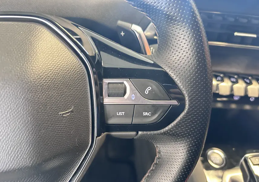 Gros plan sur les commandes gauche du volant en cuir perforé du Peugeot 3008 blanc nacré, avec tableau de bord en arrière-plan.