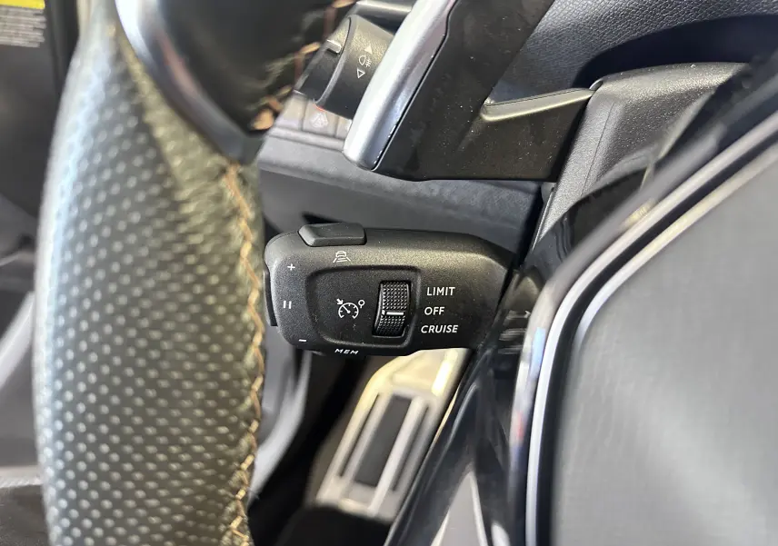 Gros plan sur la commande de régulateur de vitesse à gauche du volant cuir perforé du Peugeot 3008 blanc nacré 2022.