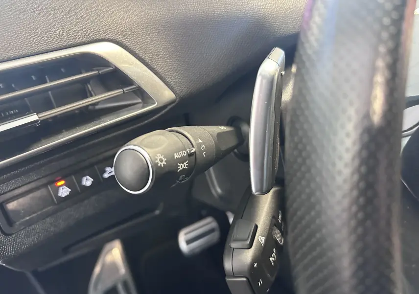 Détail intérieur du Peugeot 3008 2022 montrant la commande des phares et le volant en cuir perforé côté gauche.
