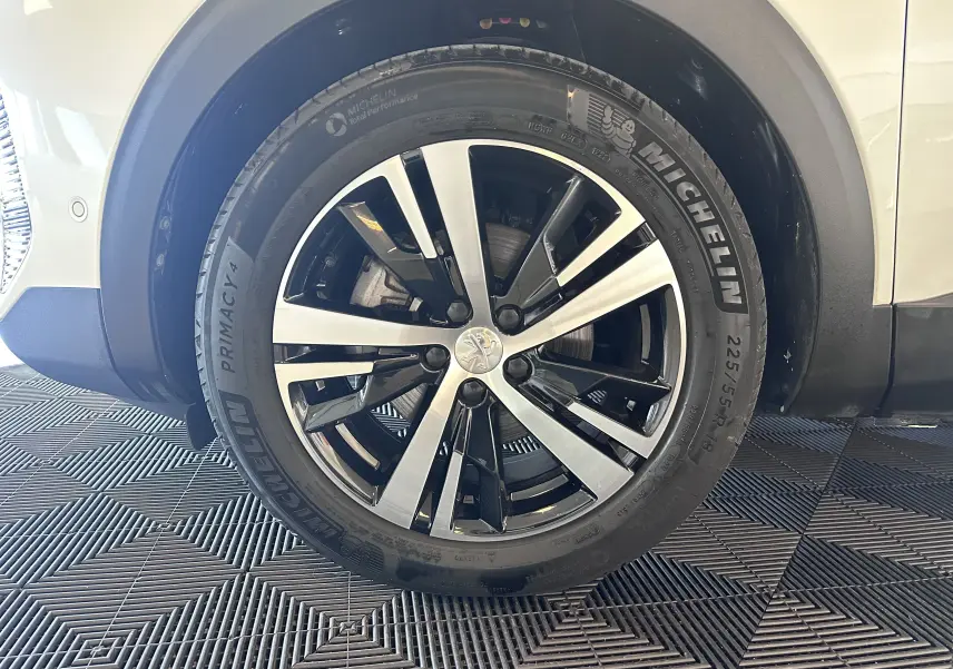 Gros plan sur la roue avant droite d’un Peugeot 3008 blanc nacré, jante alliage bicolore et pneu Michelin.