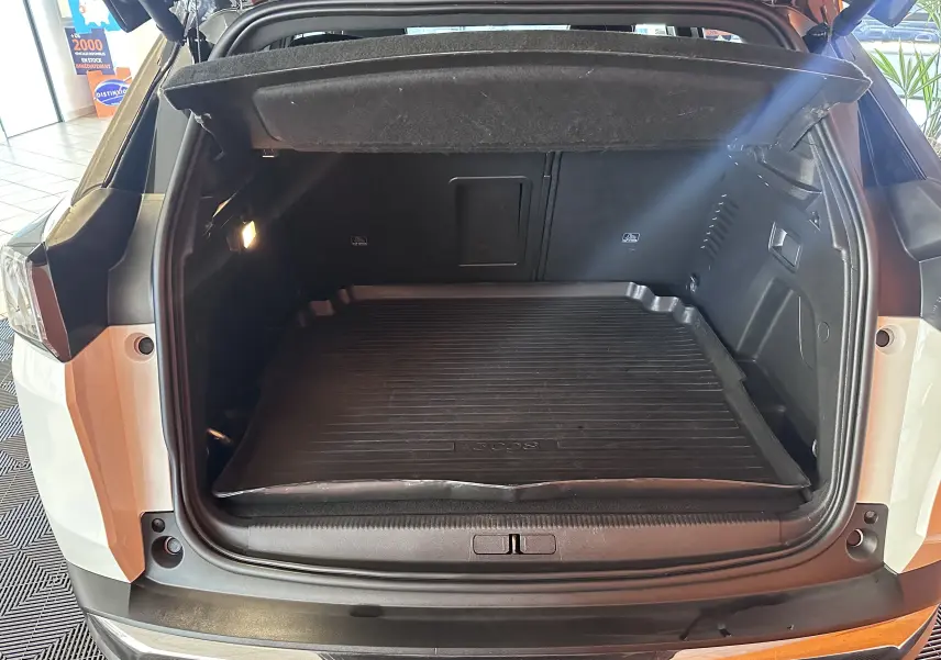 Coffre ouvert vu de l'arrière d'un Peugeot 3008 blanc nacré, avec tapis de coffre noir et intérieur spacieux.