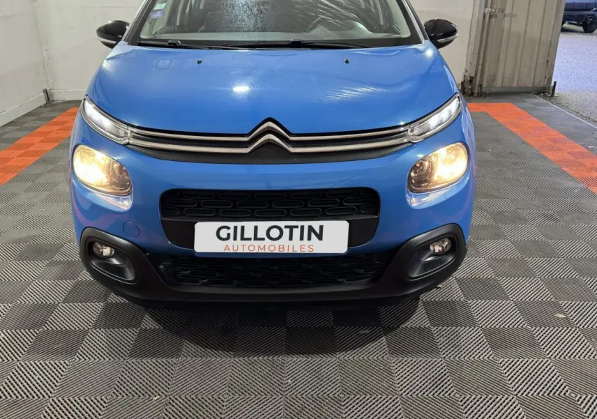 Vue avant d'une Citroën C3 bleu avec phares allumés et calandre noire dans un garage.
