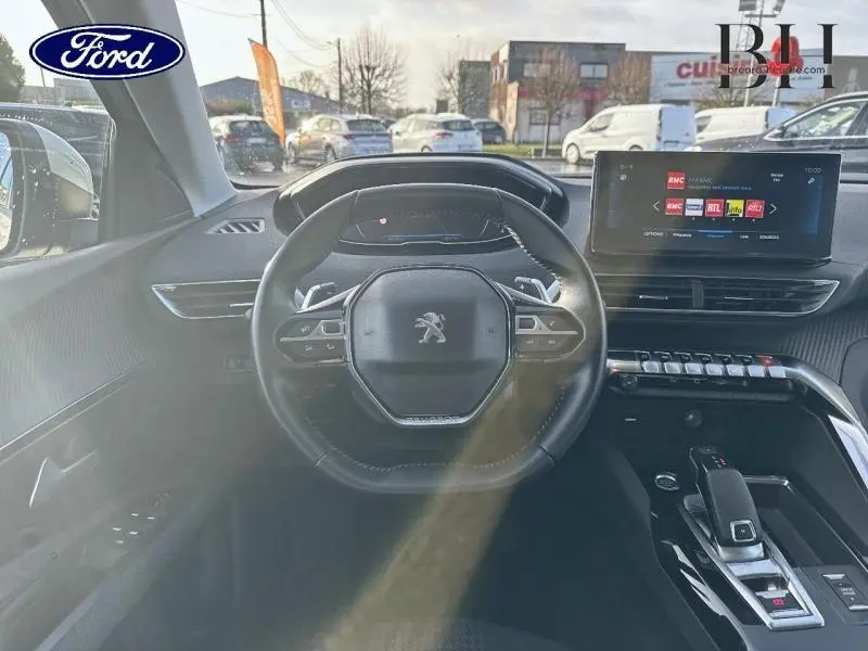 Vue intérieure centrée sur le volant cuir multifonction d'une Peugeot 5008 blanche avec écran tactile et console moderne.