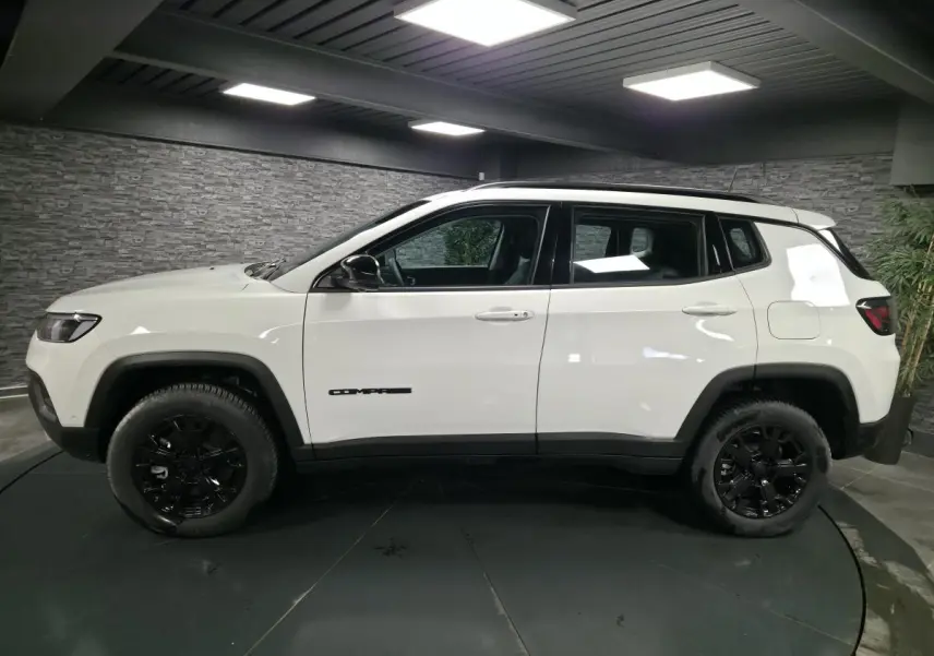 Vue de profil côté gauche d'un Jeep Compass blanc avec jantes noires et détails noirs contrastants en intérieur.