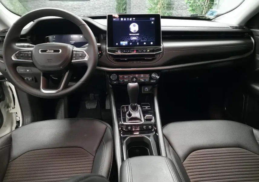 Vue intérieure avant du Jeep Compass 2024, tableau de bord noir avec écran tactile central et volant multifonction.