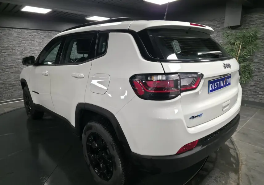 Jeep Compass blanc vue 3/4 arrière droit avec jantes noires et badges 4xe eAWD visibles.