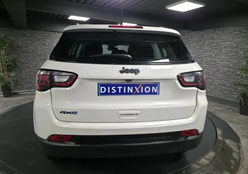 Vue arrière d’un Jeep Compass blanc hybride rechargeable avec logo 4xe et feux arrière LED dans un showroom.