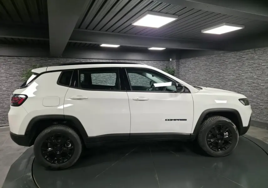 Jeep Compass blanc vu de profil côté gauche, avec jantes noires et toit noir dans un garage.