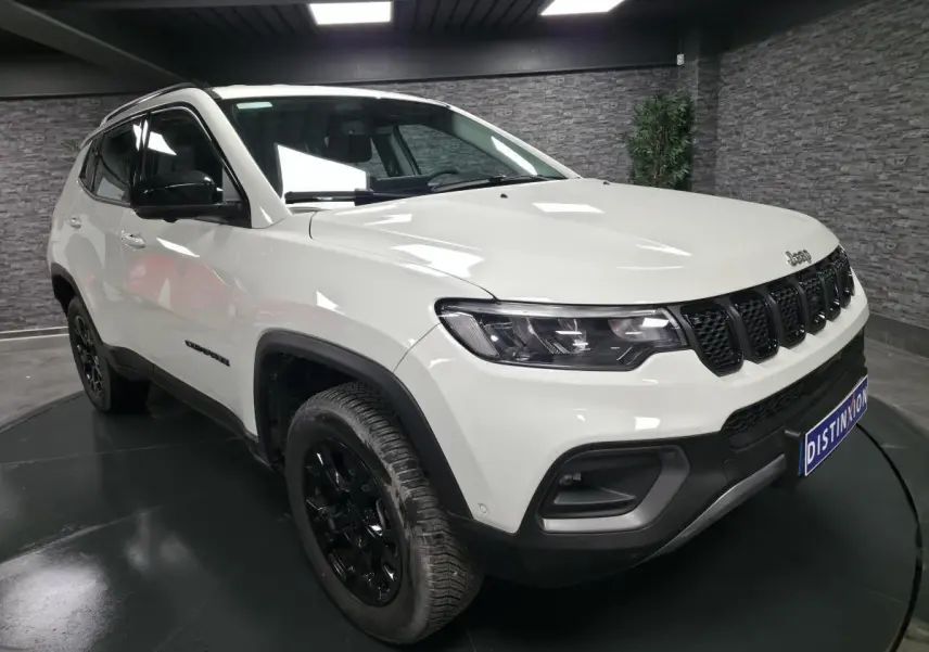 Jeep Compass blanc vue 3/4 avant droit avec jantes noires et calandre distinctive en intérieur showroom.
