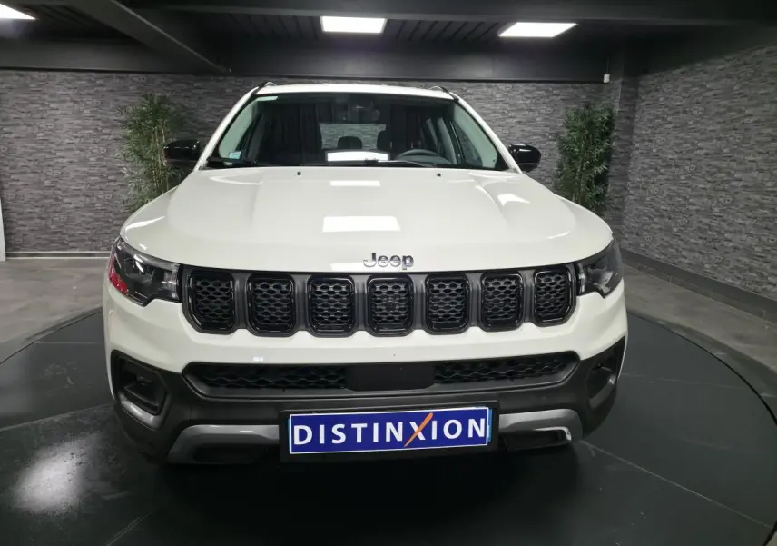 Vue frontale d'un Jeep Compass blanc avec calandre noire et logo Jeep visible sur fond intérieur gris.