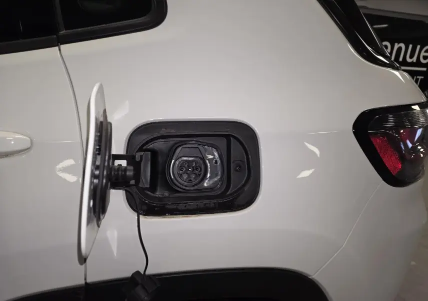Prise de recharge ouverte côté gauche arrière d’un Jeep Compass blanc avec câble visible et feu arrière partiel.
