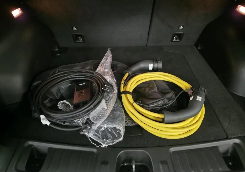 Vue du coffre du Jeep Compass 2024 avec câbles de recharge noir et jaune posés sur la moquette noire.