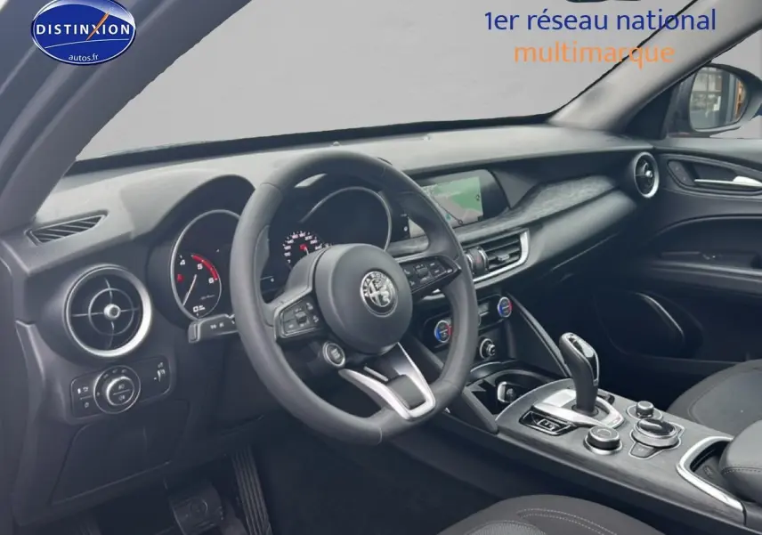 Vue intérieure côté conducteur de l'Alfa Romeo Stelvio gris Vesuvio, volant cuir multifonction et écran tactile central.