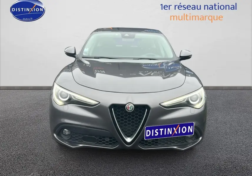 Vue avant d'une Alfa Romeo Stelvio gris vesuvio metal avec phares allumés et calandre caractéristique en V.