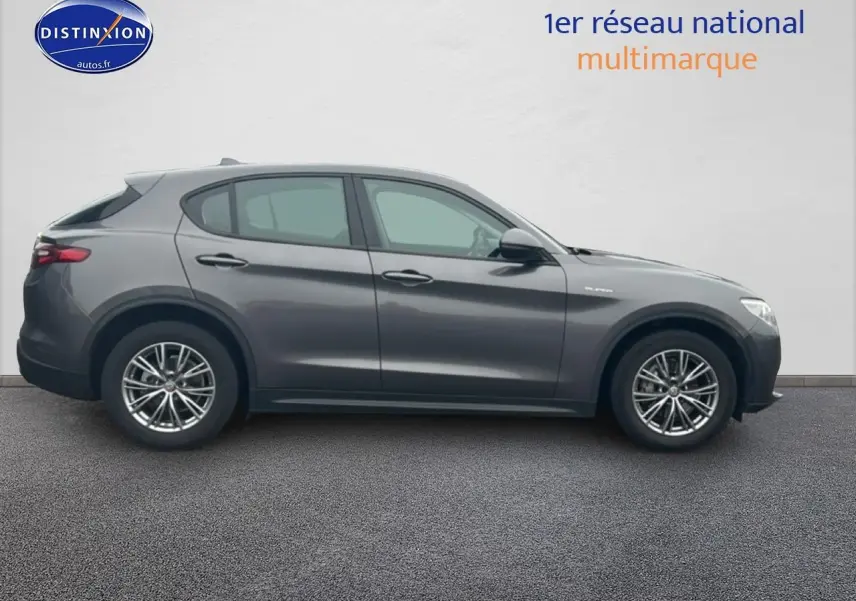 Vue de profil côté gauche d'un Alfa Romeo Stelvio gris vesuvio metal avec jantes alu multibranches.