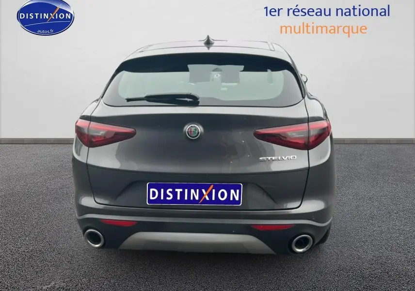 Vue arrière d'un Alfa Romeo Stelvio gris vesuvio metal avec double sortie d'échappement et feux arrière LED.