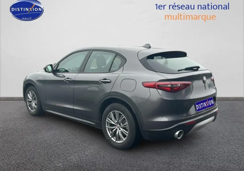 Vue 3/4 arrière droite d'un Alfa Romeo Stelvio gris Vesuvio metal avec échappement double et jantes alu.