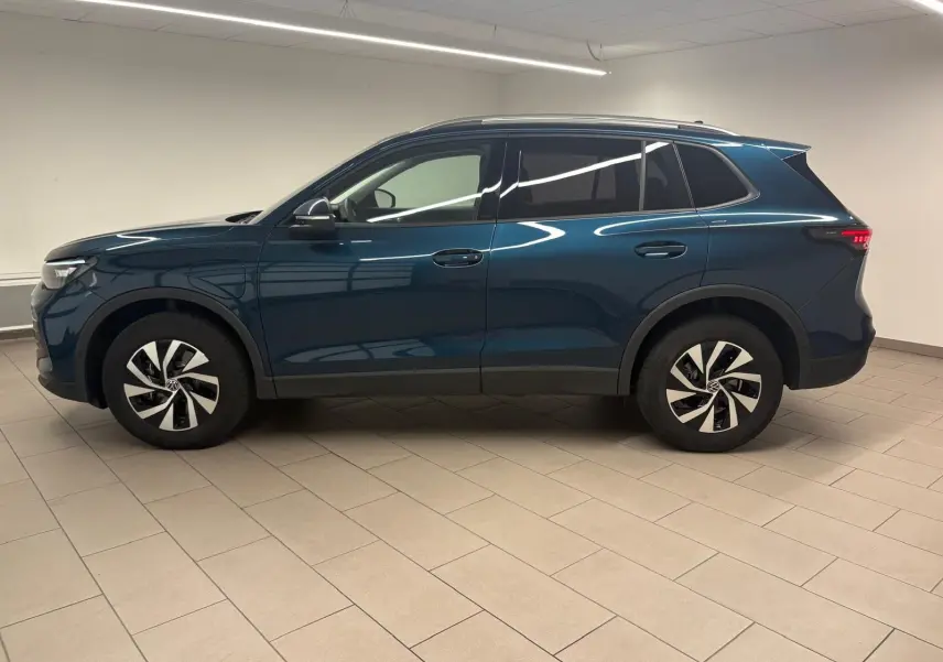 Vue de profil côté gauche du Volkswagen Tiguan 1.5 eHybrid TSI 204 DSG6 en bleu Nightshade métallisé, intérieur lumineux.