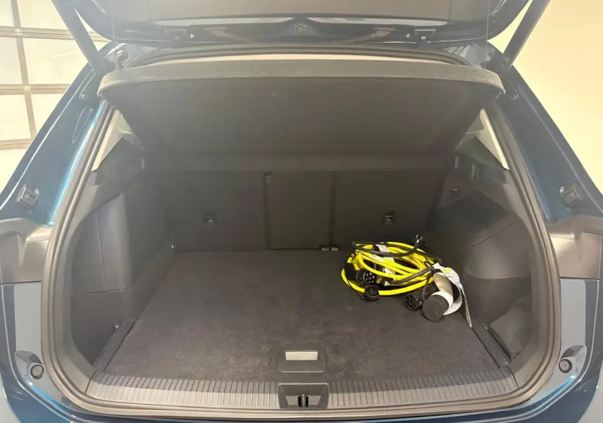 Coffre ouvert du Volkswagen Tiguan 1.5 eHybrid en Nightshade Blue, montrant un câble de recharge jaune dans un espace spacieux.