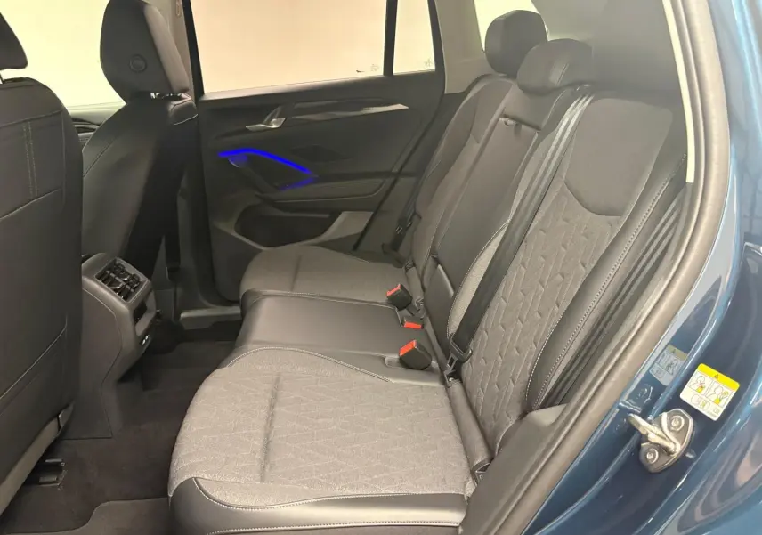 Vue intérieure côté droit des sièges arrière du Volkswagen Tiguan 1.5 eHybrid en Nightshade Blue avec éclairage d'ambiance bleu sur la portière.