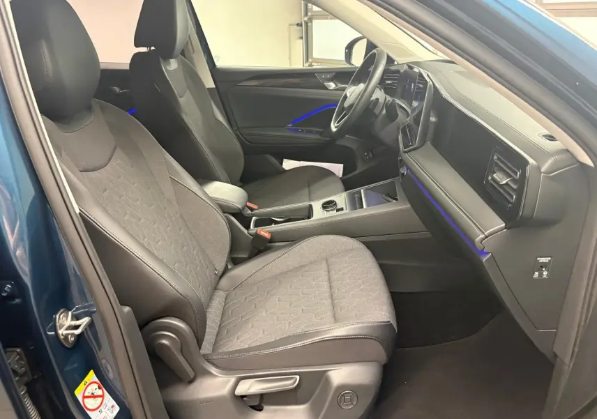 Intérieur avant droit du Volkswagen Tiguan 1.5 eHybrid Nightshade Blue avec sièges chauffants et éclairage d'ambiance bleu.