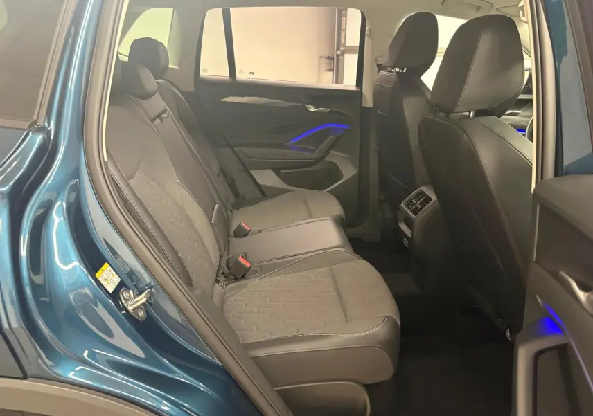 Vue intérieure arrière droite du Volkswagen Tiguan 2025 Nightshade Blue, sièges tissu et cuir, éclairage d'ambiance bleu sur les portes.