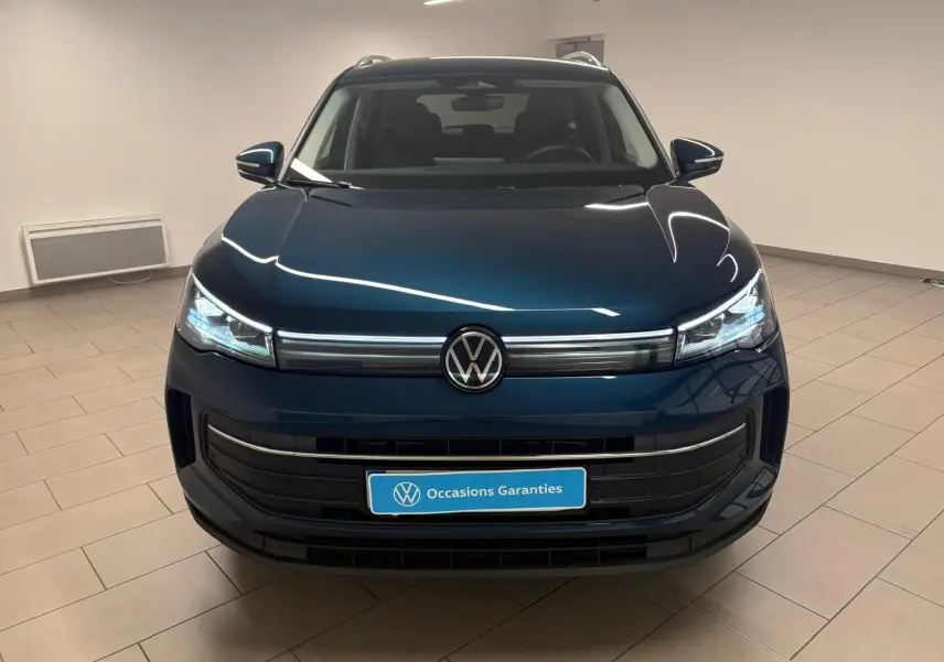 Vue frontale du Volkswagen Tiguan 1.5 eHybrid TSI 204 DSG6 en bleu Nightshade, avec phares LED allumés dans un showroom.