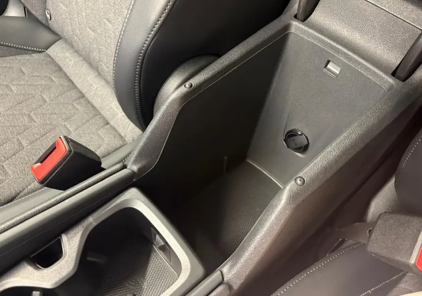 Vue rapprochée de la console centrale ouverte du Volkswagen Tiguan 2025, montrant le rangement intérieur et les sièges gris et noirs.