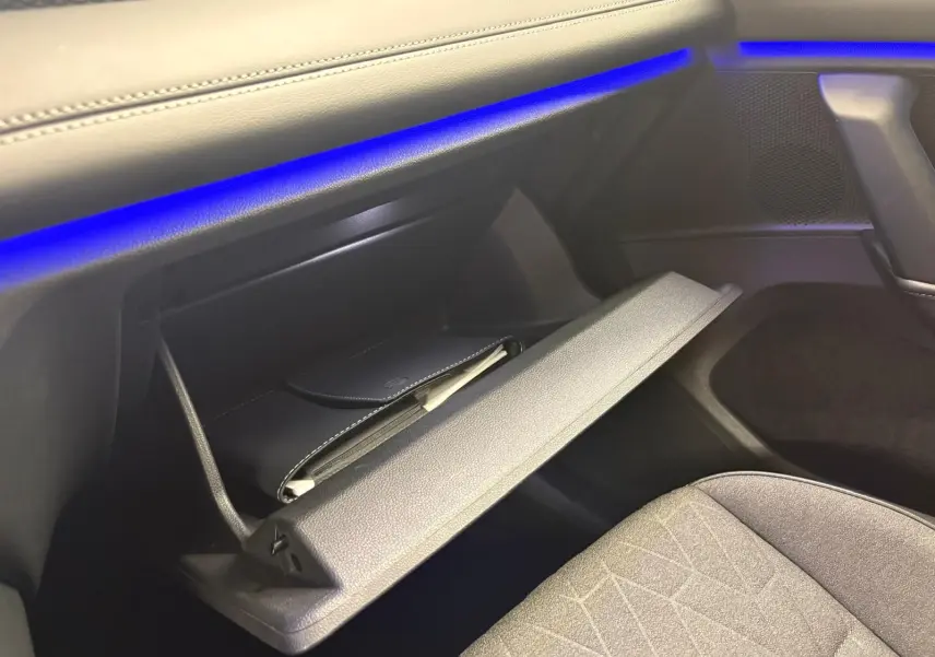 Gant de boîte à gants ouvert côté passager avec éclairage d'ambiance bleu sur tableau de bord du Volkswagen Tiguan 2025.