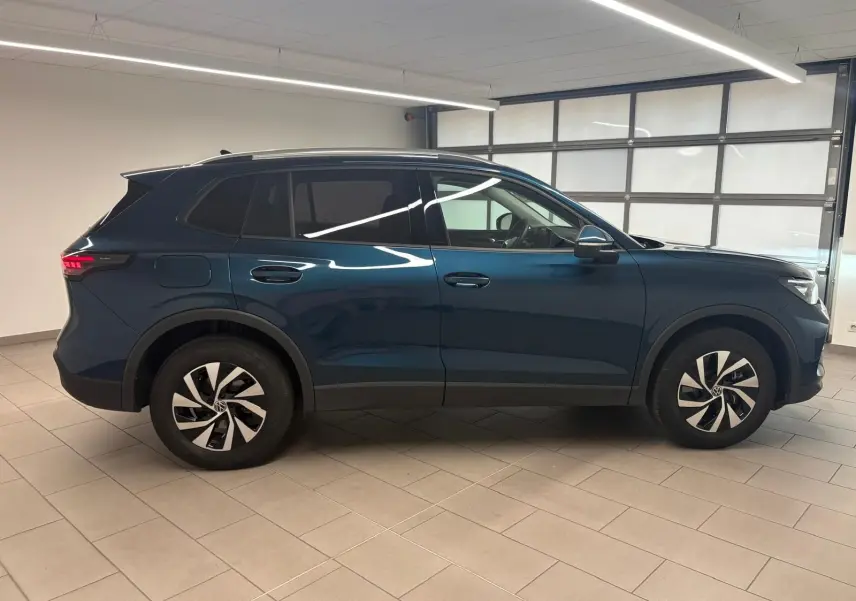 Vue de profil côté gauche du Volkswagen Tiguan 1.5 eHybrid TSI 204 DSG6 en bleu métallisé Nightshade, intérieur visible par les vitres teintées.