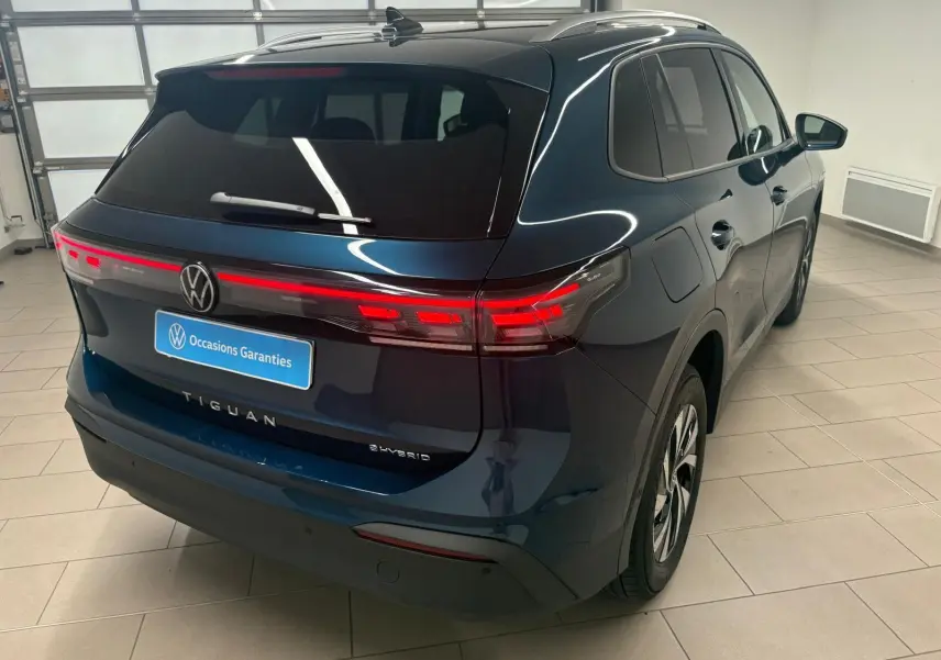 Vue 3/4 arrière droite du Volkswagen Tiguan 1.5 eHybrid TSI 204 DSG6 en bleu Nightshade, avec feux arrière allumés.
