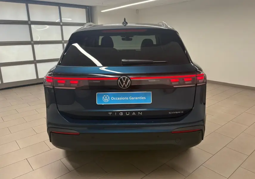 Vue arrière du Volkswagen Tiguan hybride rechargeable 2025 en Nightshade Blue, avec feux arrière LED allumés dans un garage.
