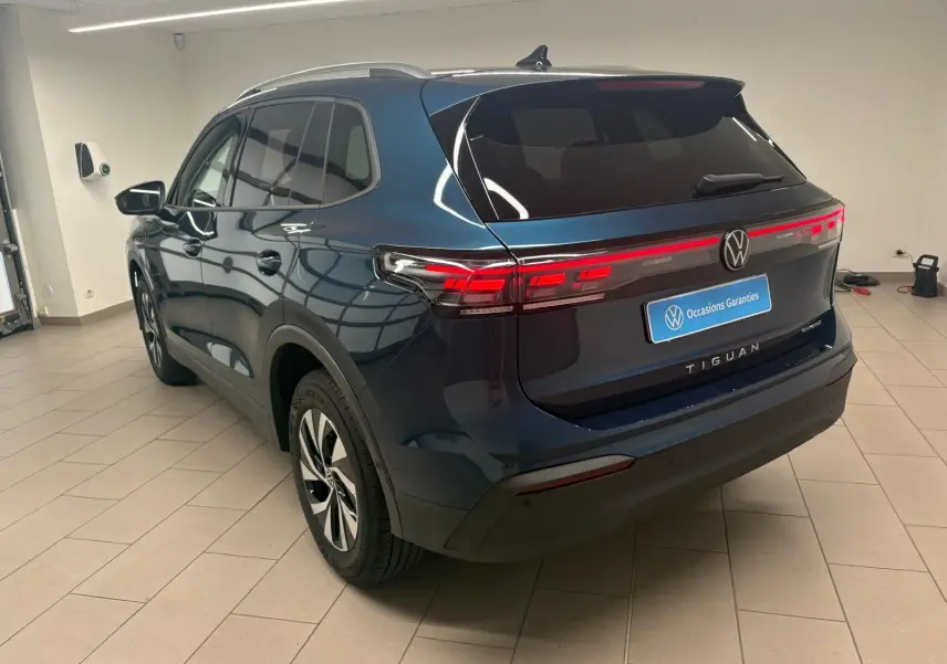 Vue 3/4 arrière droite du Volkswagen Tiguan 1.5 eHybrid TSI 204 DSG6 en bleu Nightshade, avec feux arrière allumés.