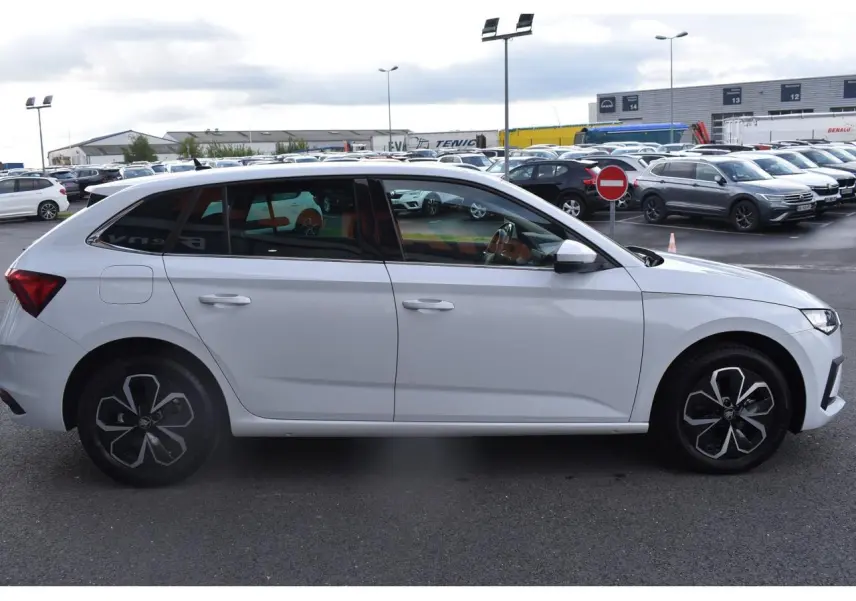 Vue latérale droite d'une Skoda Scala blanc glacier avec jantes alliage noires et détails modernes sur parking.