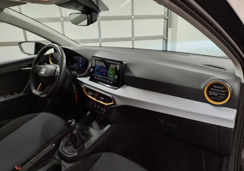 Intérieur de la SEAT Ibiza 2024 noir minuit, vue côté conducteur montrant tableau de bord avec écran tactile et détails orange.