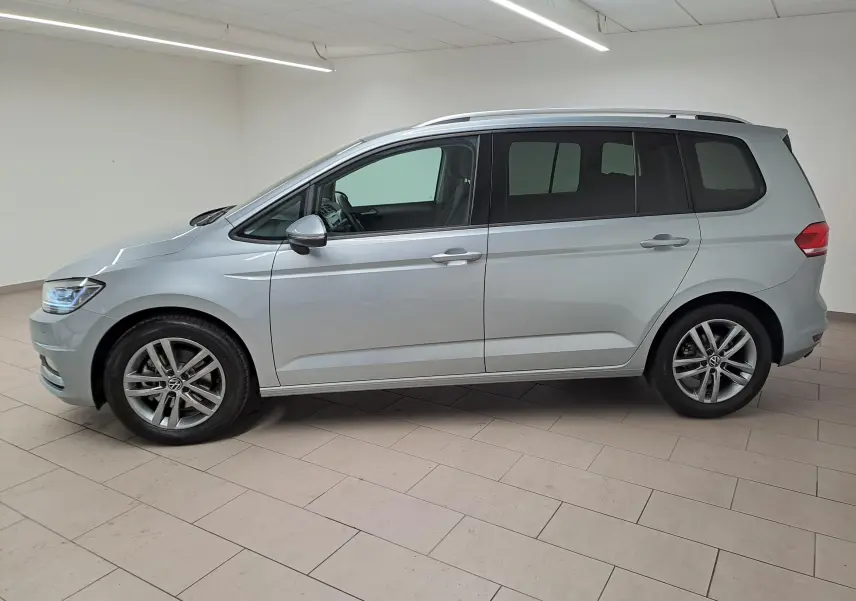Vue de profil côté gauche d'un Volkswagen Touran 2025 en peinture métallisée Argent Dolomite dans un intérieur neutre.