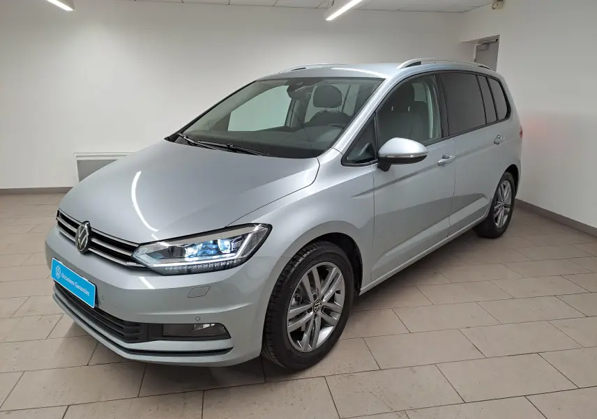 Volkswagen Touran 2025 argent Dolomite en 3/4 avant droit, avec phares LED allumés et jantes alliage.