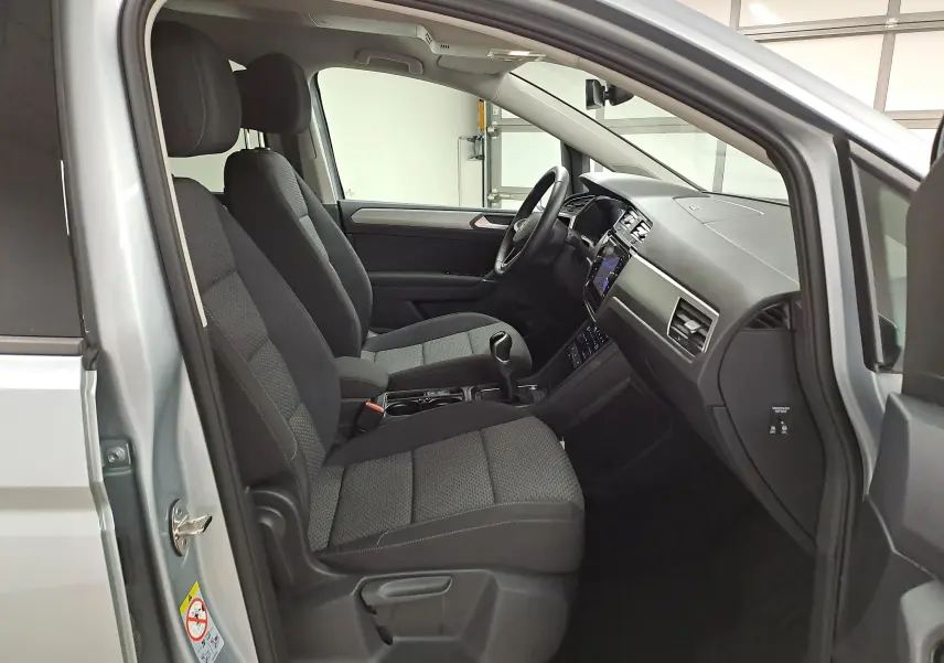 Vue intérieure côté conducteur du Volkswagen Touran 2025 argent Dolomite, sièges tissu gris et tableau de bord moderne.