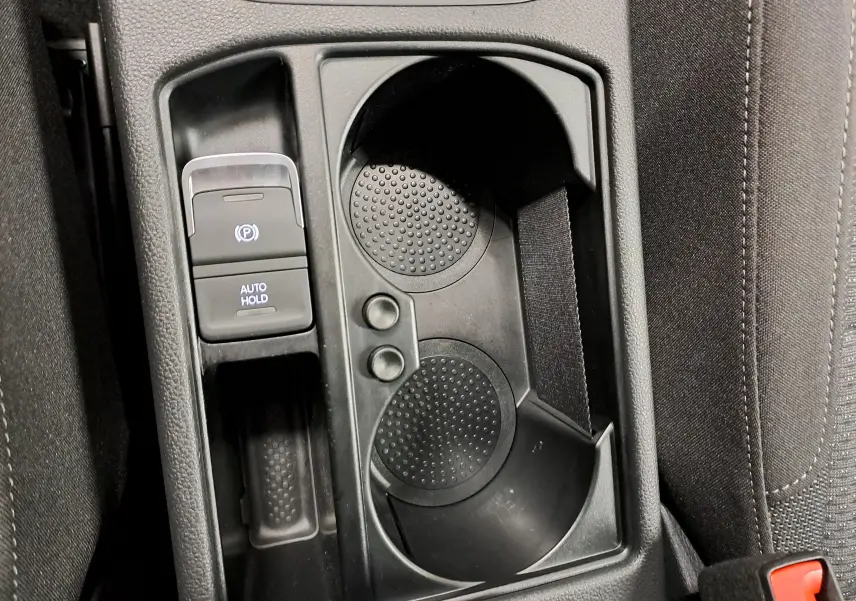 Gros plan sur la console centrale noire du Volkswagen Touran 2025, avec porte-gobelets et bouton frein à main électrique.