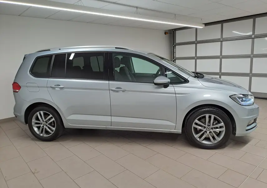 Vue de profil côté gauche d'un Volkswagen Touran 2025 en peinture métallisée Argent Dolomite dans un garage.