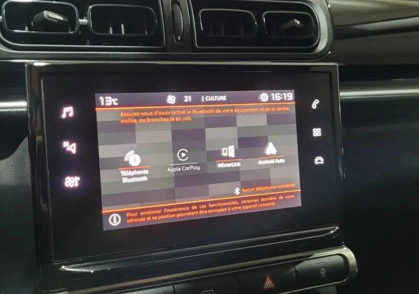 Écran tactile central allumé dans l’habitacle noir d’une Citroën C3 beige, vue de face rapprochée.