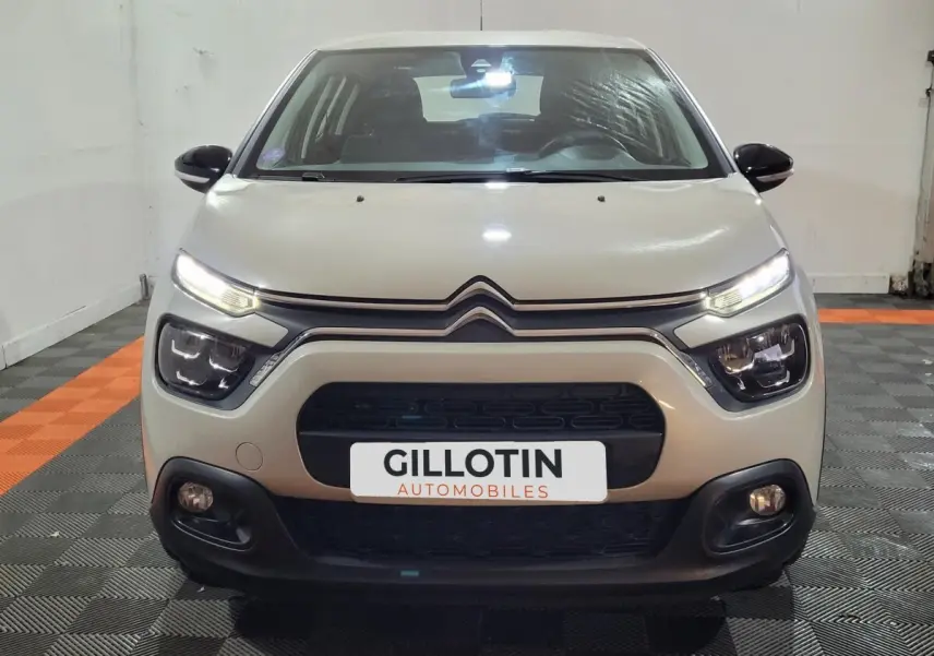 Vue frontale d'une Citroën C3 beige 2022 avec feux LED allumés dans un garage intérieur.