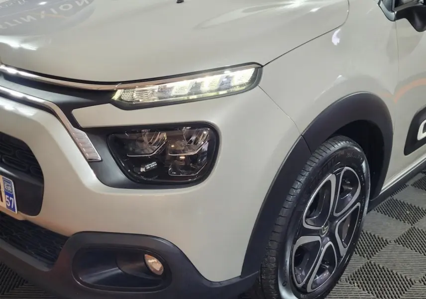 Vue 3/4 avant droit d'une Citroën C3 beige 2022 avec phares LED allumés et jantes alliage distinctives.