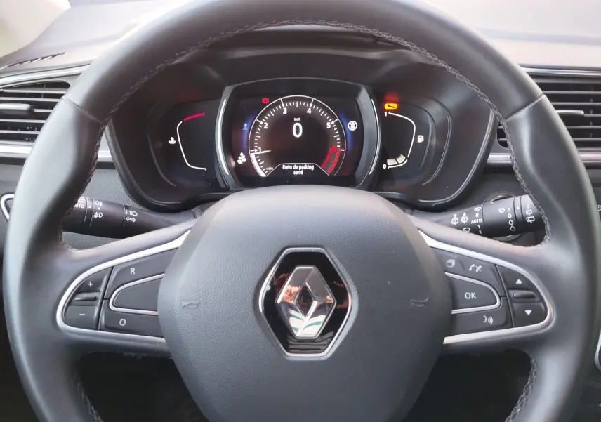 Vue rapprochée du volant noir avec logo Renault et tableau de bord numérique du Renault Kadjar gris Titanium 2021.