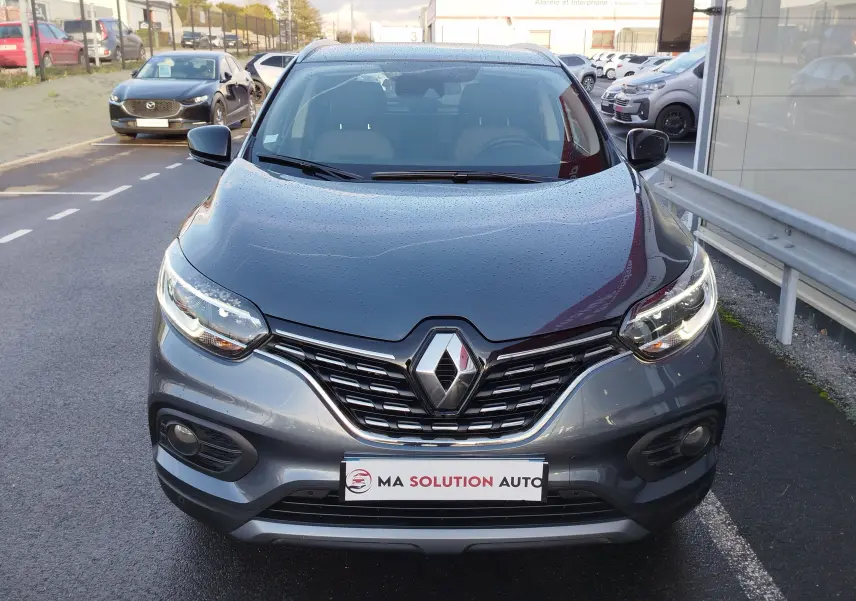 Vue avant d’un Renault Kadjar gris titanium 2021 avec calandre chromée et phares LED allumés.